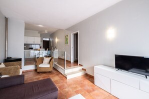 Ein modernes Wohnzimmer mit Fernseher, einer Couch und einem Korbstuhl.