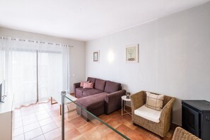 A living room with a sofa, a wicker chair, a glass coffee table, and a television. - #099 T1 Caliços by Home Holidays (Albufeira)