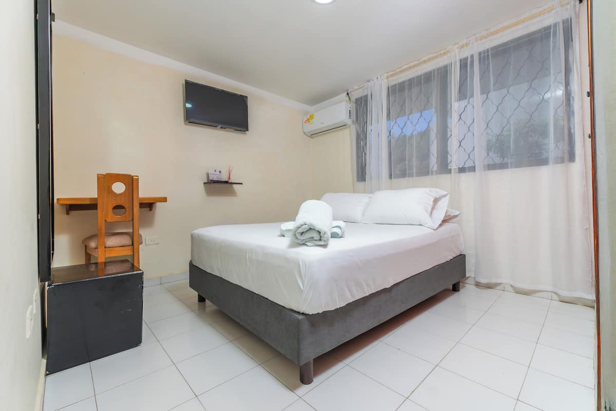 Une chambre à coucher comprenant un lit, une chaise, un téléviseur et un appareil de climatisation.
