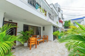A courtyard with a wooden bench and chairs, surrounded by potted plants and a white building with balconies.