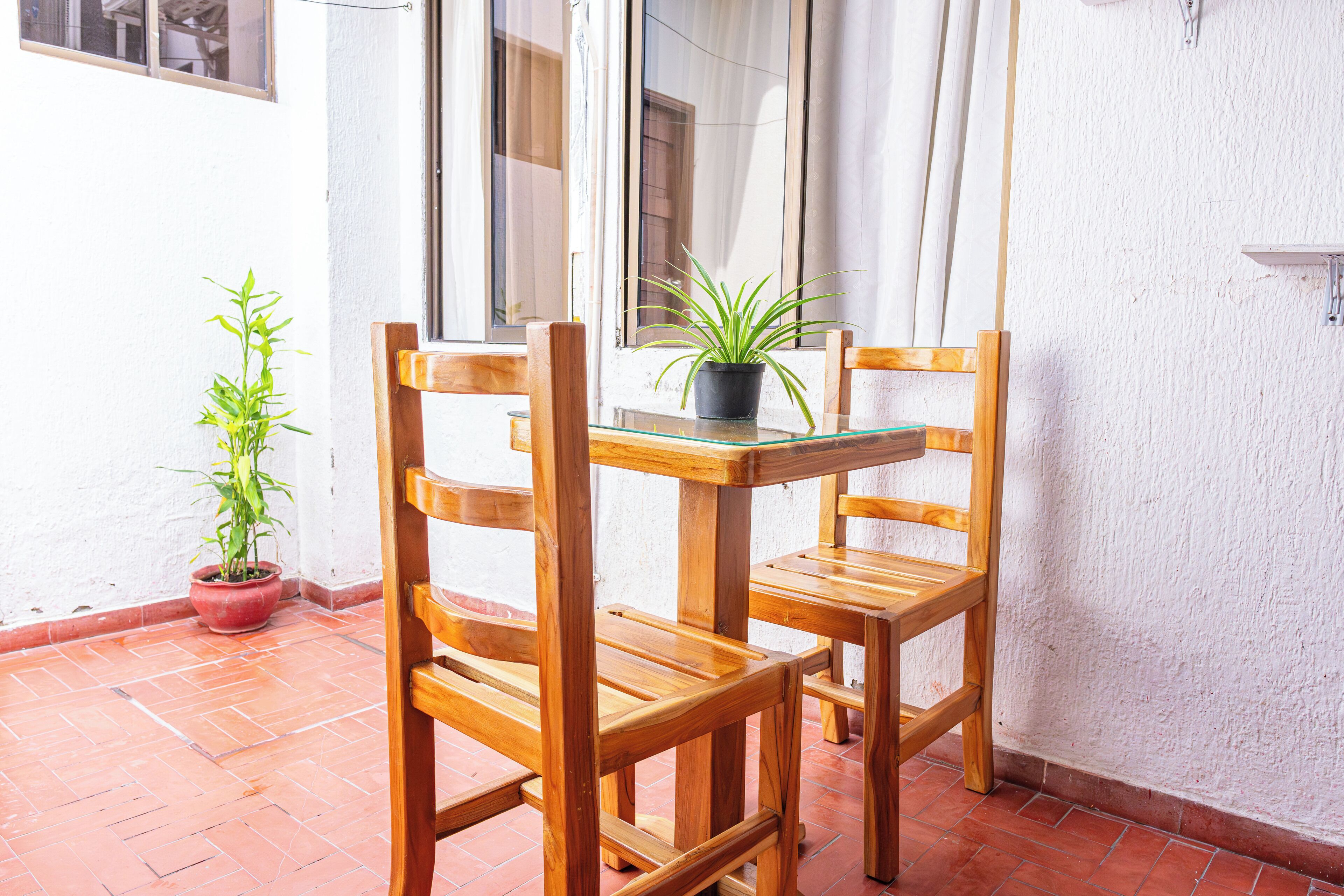 A wooden table and chairs set on a tiled patio with potted plants.