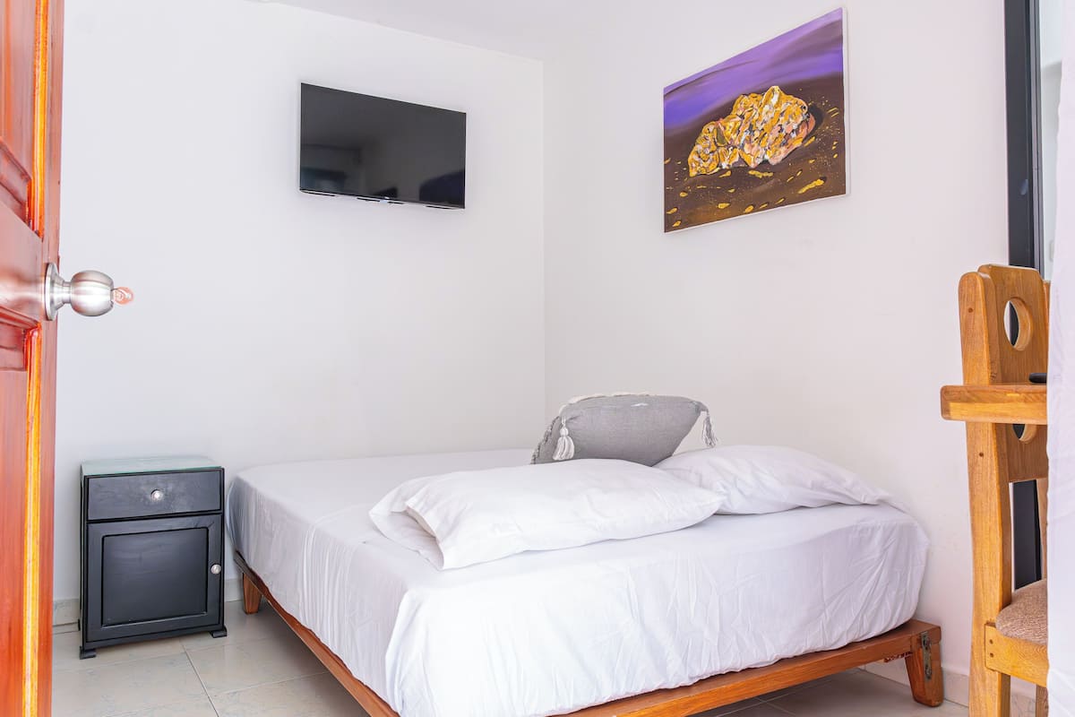 Une chambre à coucher avec un lit, un téléviseur fixé au mur et un tableau au-dessus du lit.