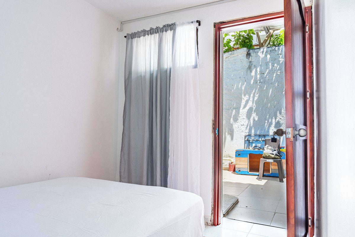A room with a bed, a sliding glass door leading to an outdoor area with a blue chair and a wooden bench.