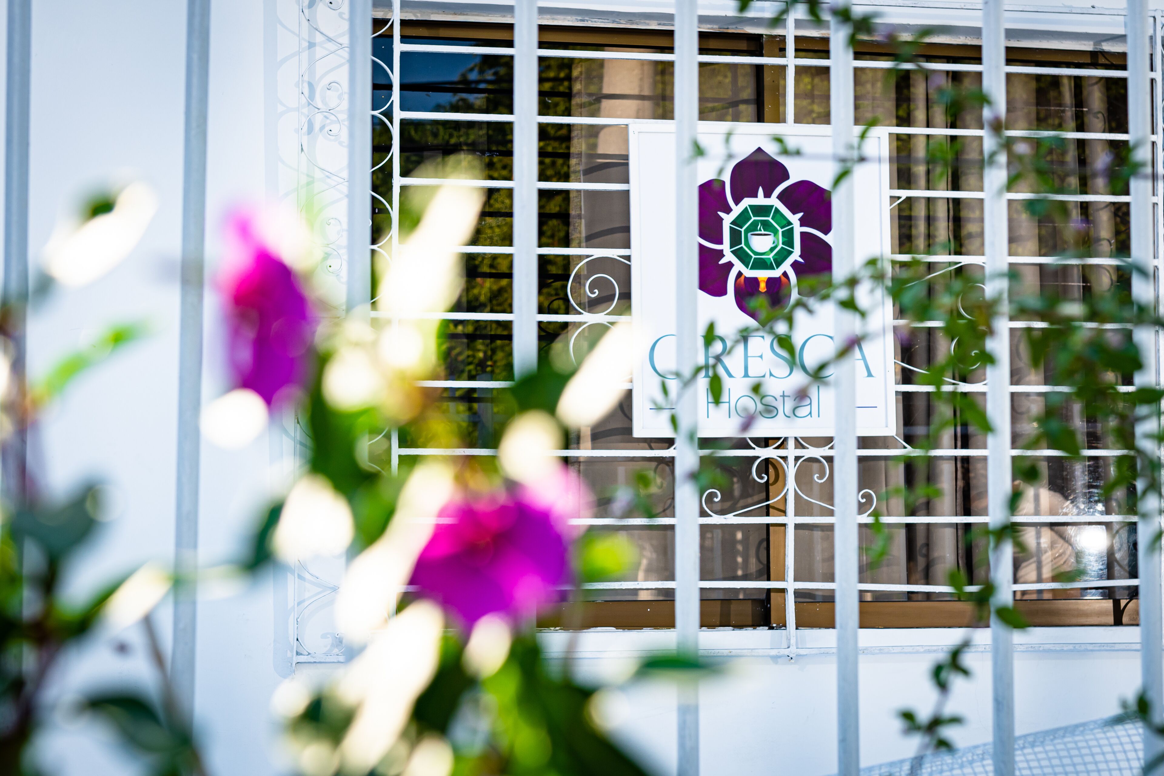 Une fenêtre avec une enseigne indiquant « CRESCA Hostal » et une grille métallique décorative.