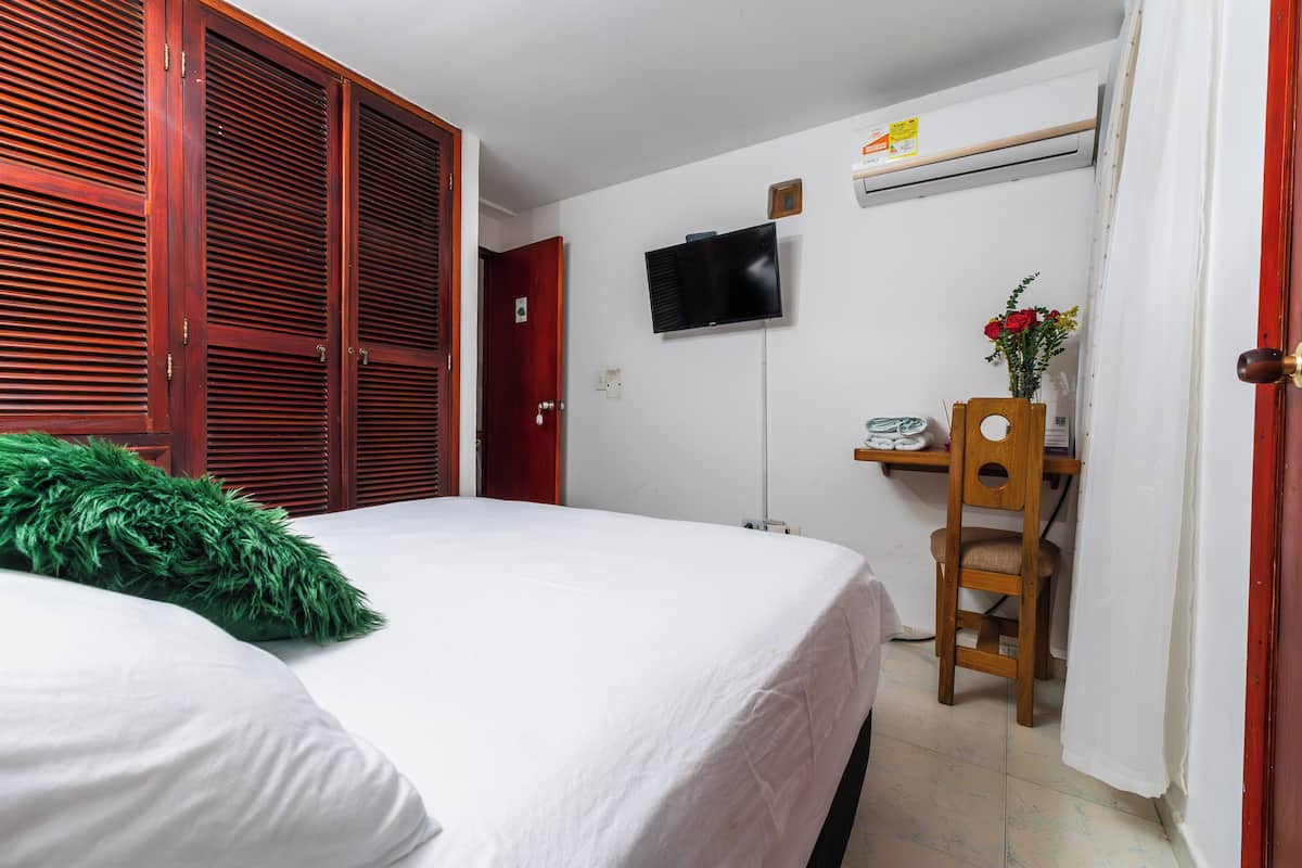 Une chambre à coucher comprenant un lit, un bureau avec une chaise, une télévision et une armoire.