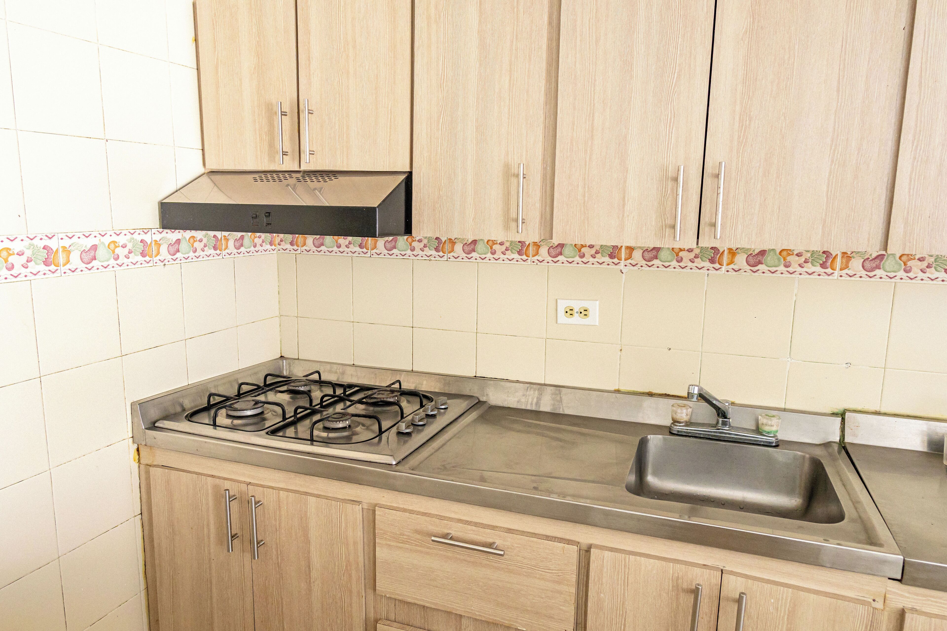 A kitchen with wooden cabinets, a gas stove, a sink, and a decorative tile border.