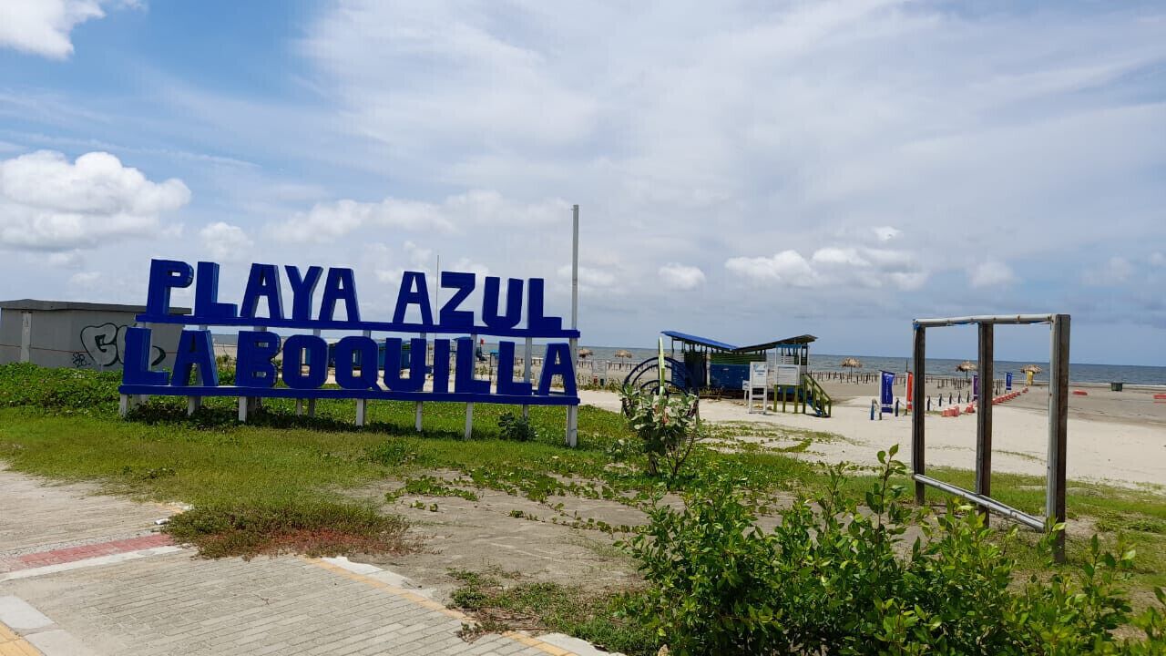 Schild für Playa Azul La Boquilla, im Hintergrund ein Strand und ein Rettungsturm.