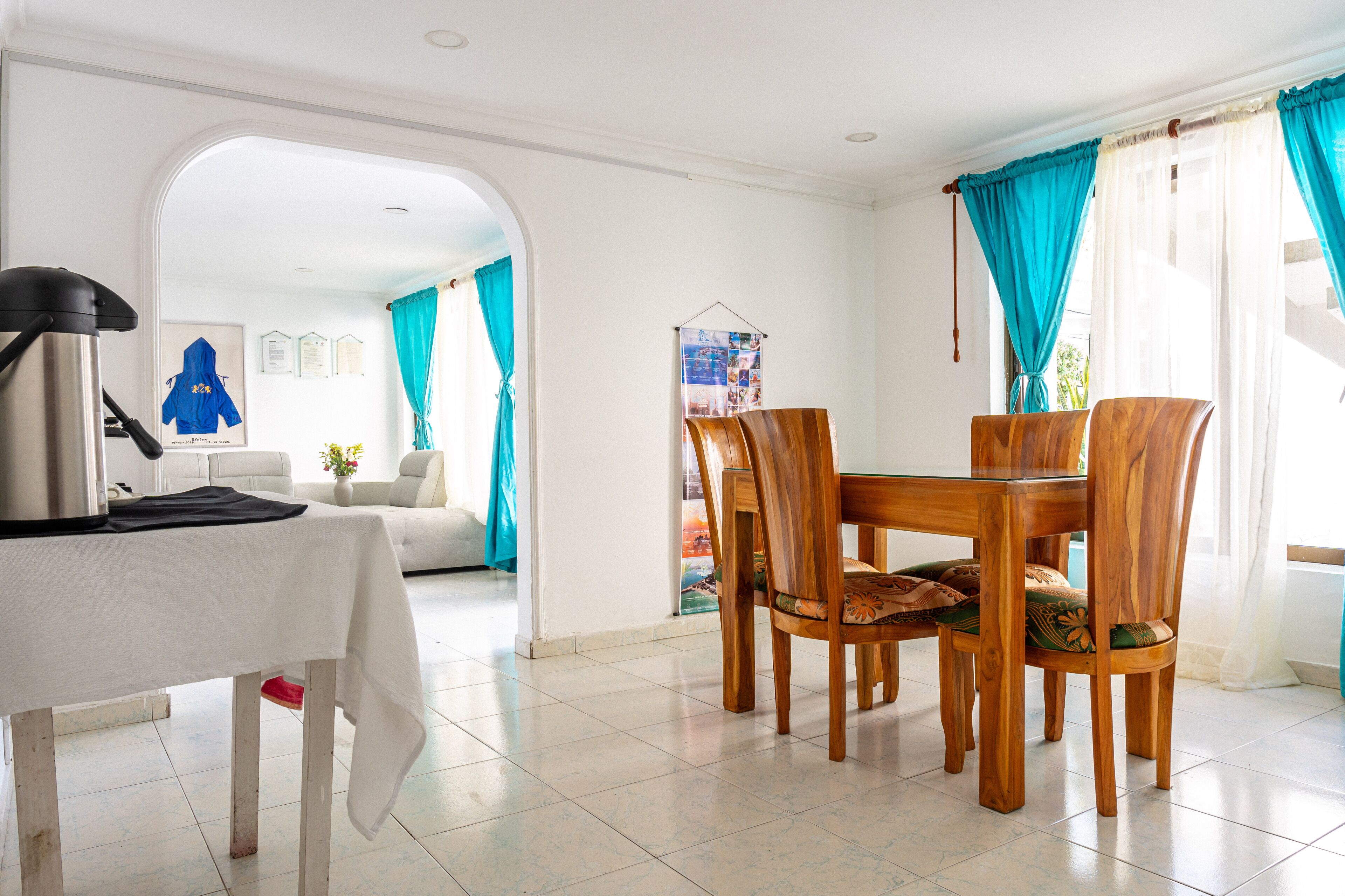 Un comedor con una mesa y sillas, una cafetera y vistas a otra habitación con un sofá y cortinas.