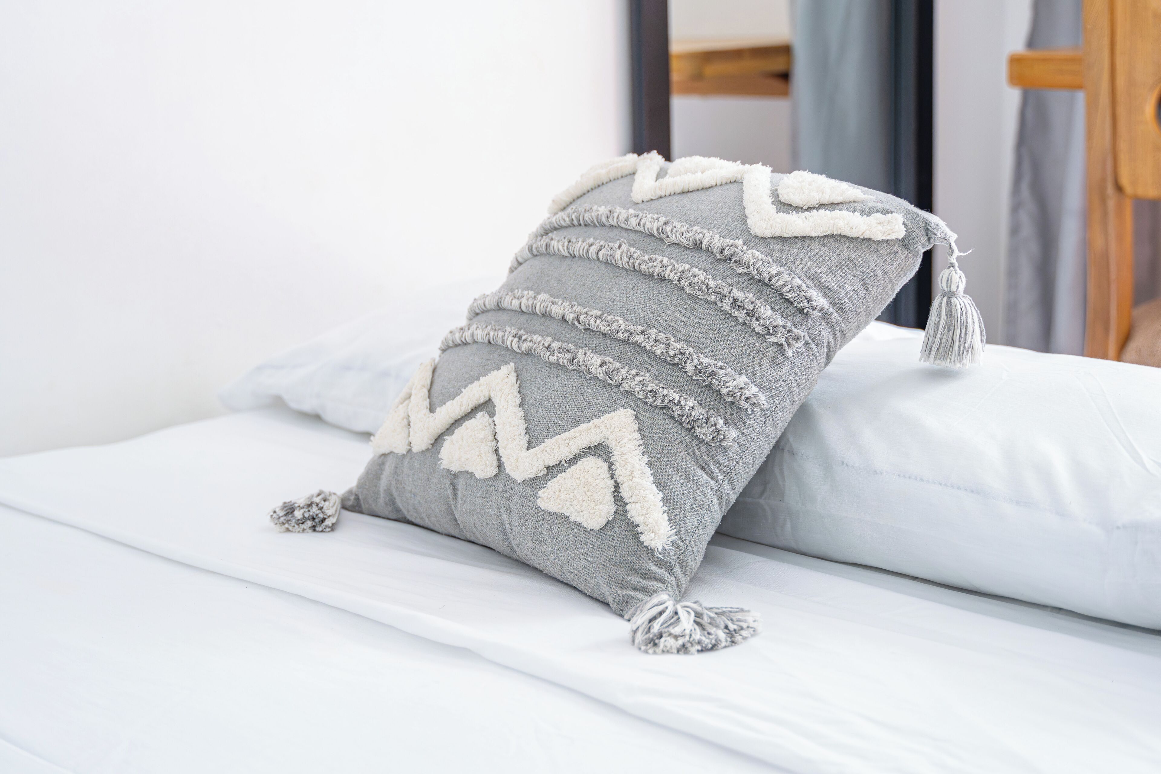 Una cama con un almohadón gris con un estampado en zigzag y flecos.