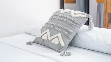A bed with a grey pillow featuring a zigzag pattern and tassels.