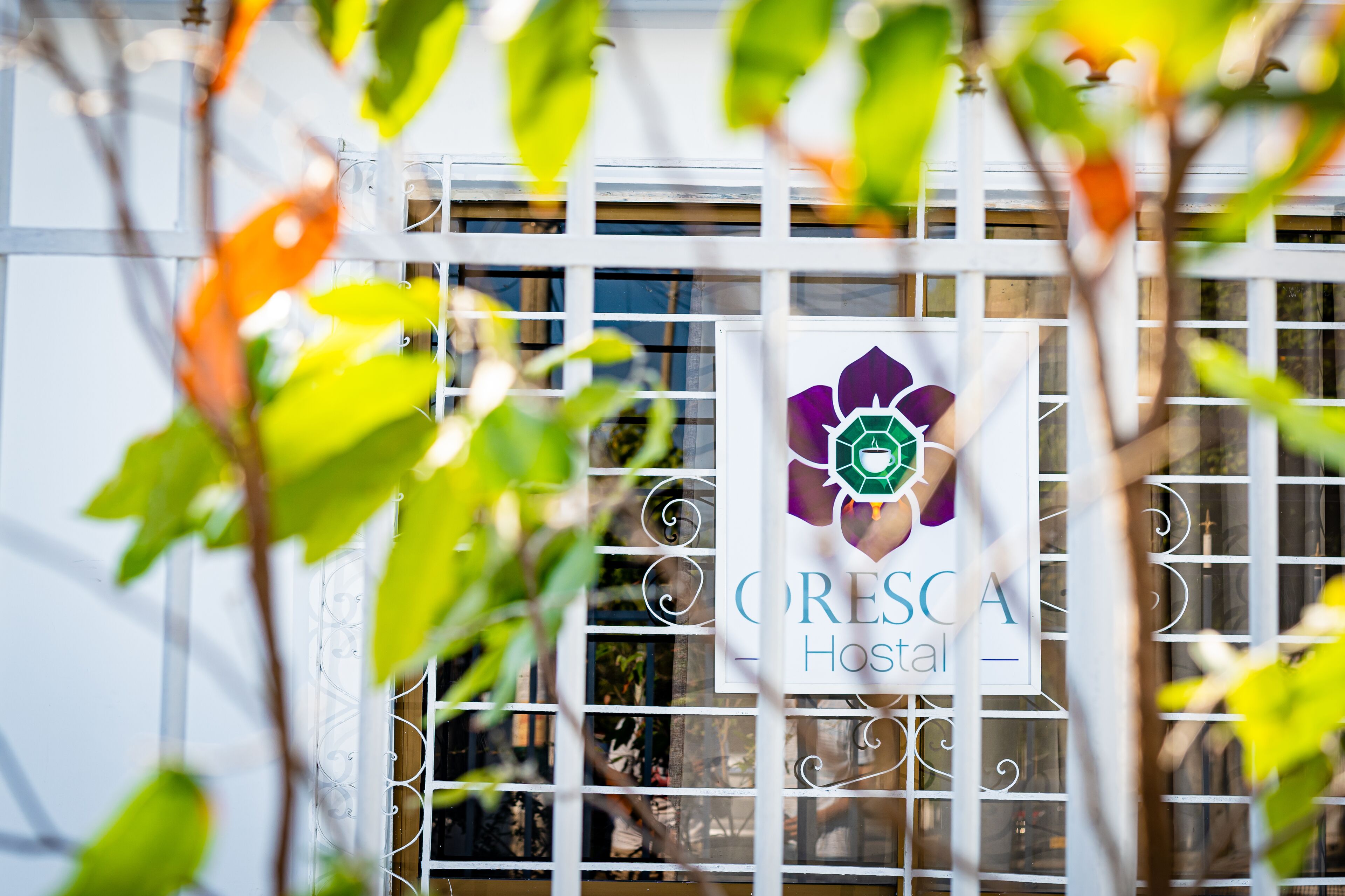 Een bord met de tekst 'CRESCA Hotel' en een logo, deels verborgen achter een metalen hek en begroeiing.