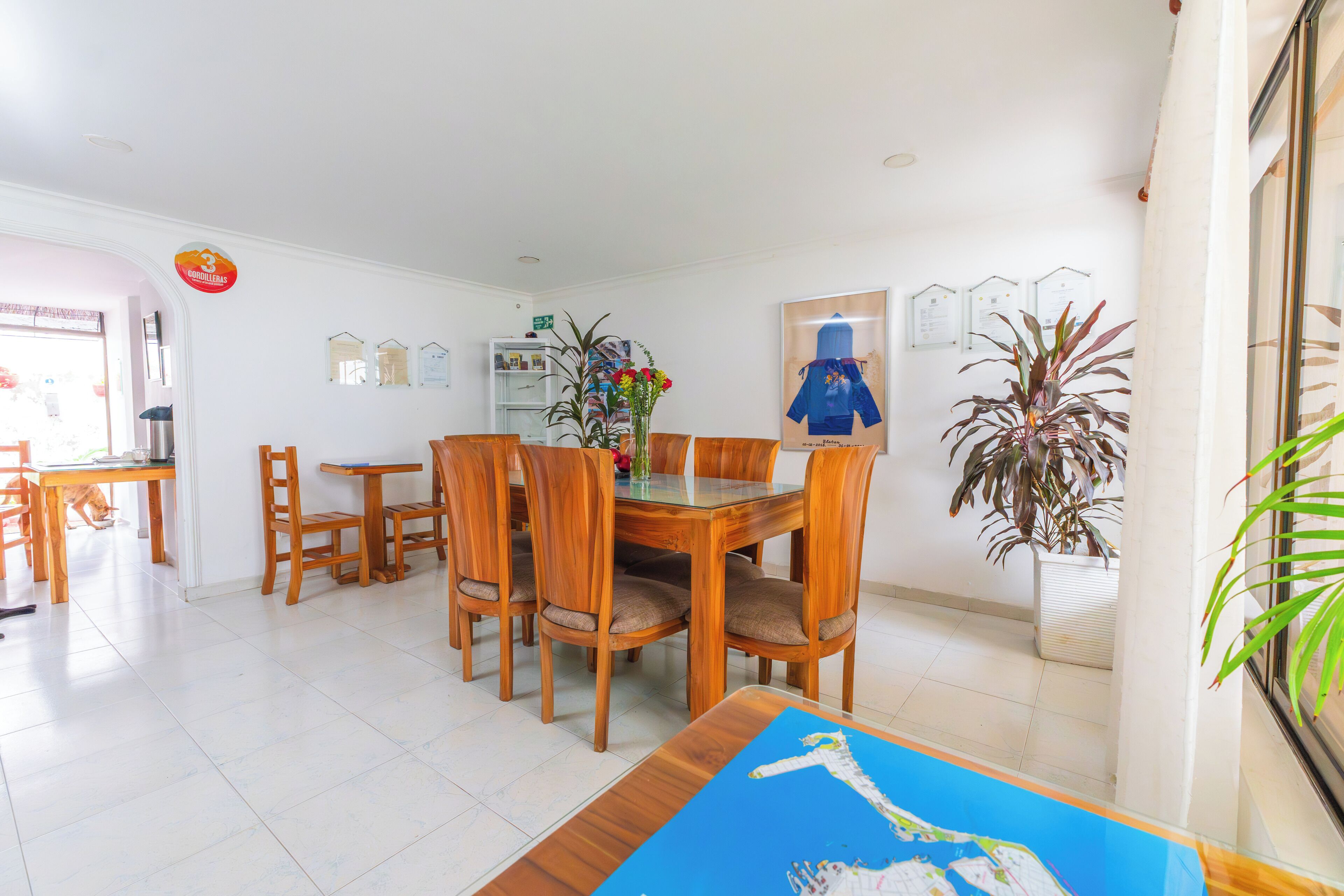 A dining area with a wooden table and chairs, a glass-top table, and a vase with flowers.