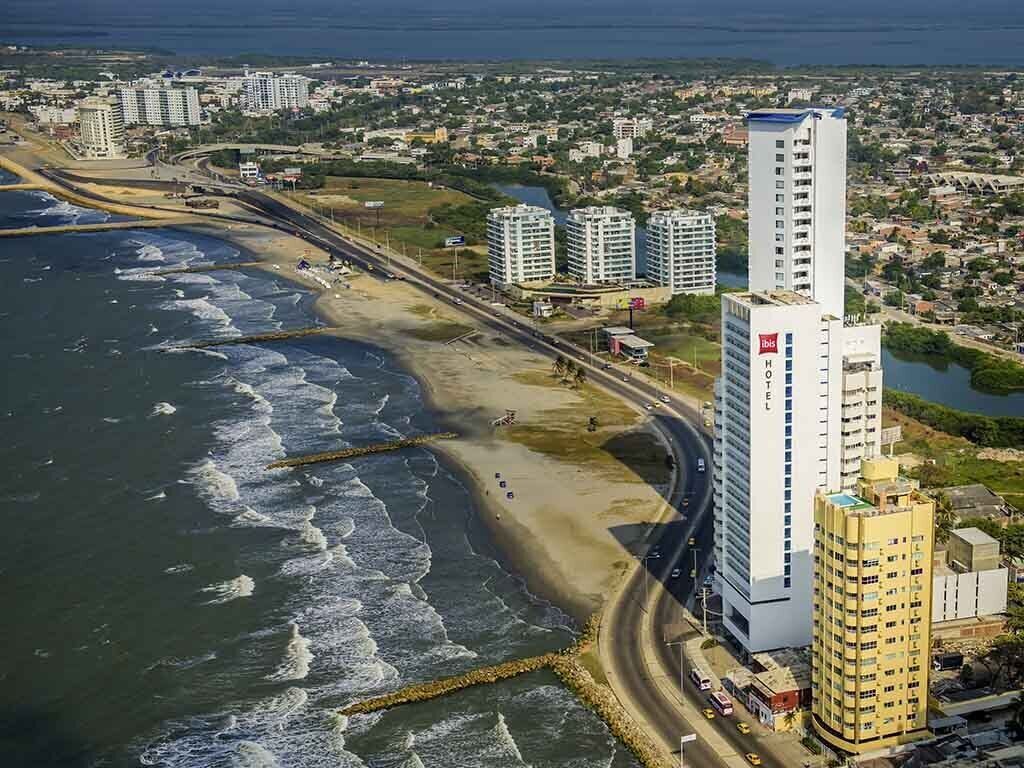 A coastal cityscape with high-rise buildings, a beach, and a road running parallel to the shore.