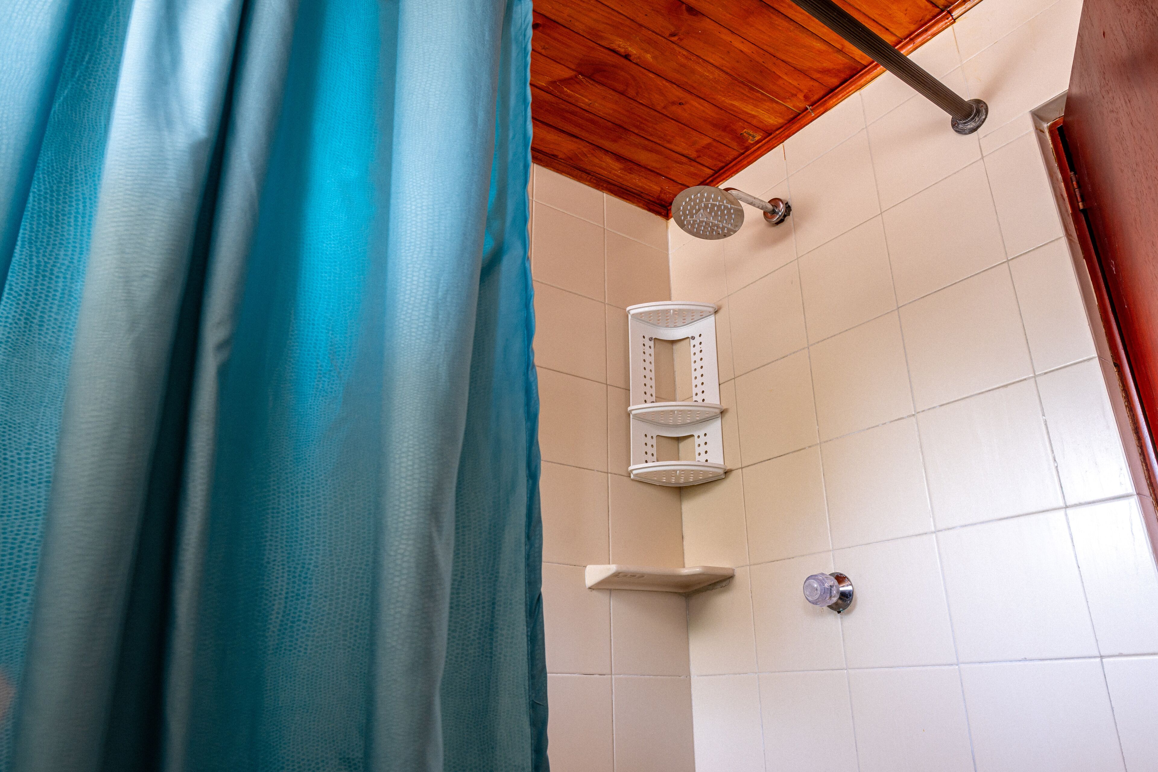 A shower area with a blue curtain, a white tiled wall, and a wooden ceiling.