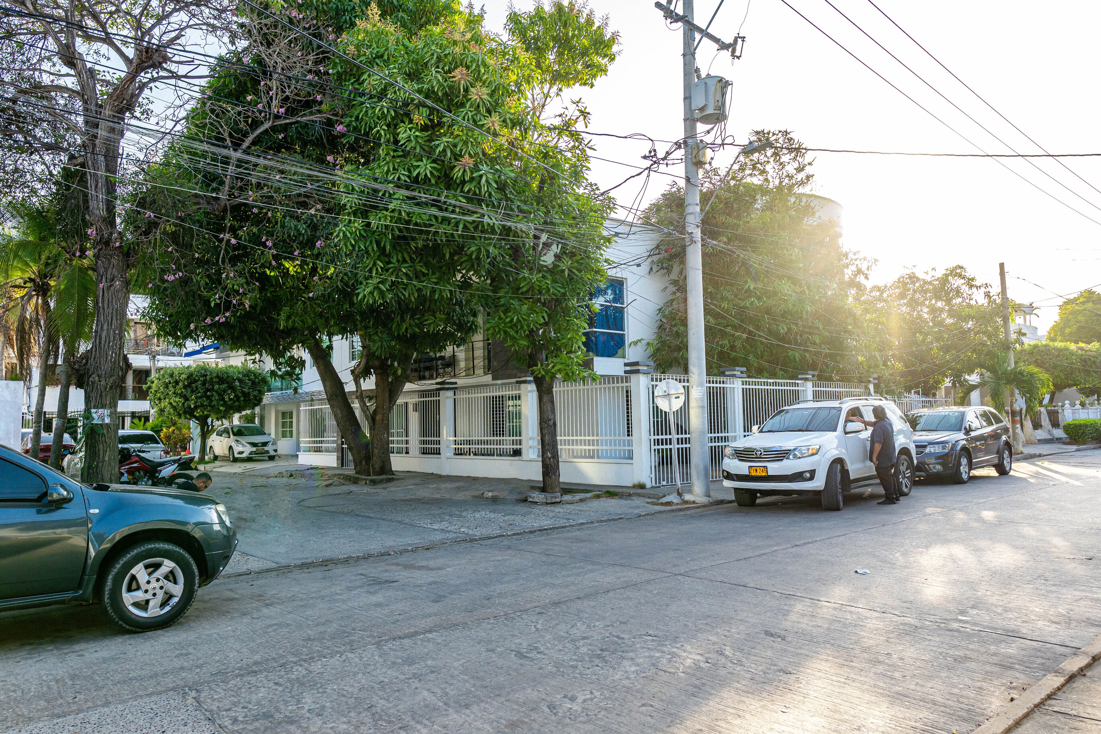 A street scene with parked cars, a gated fence, and trees.