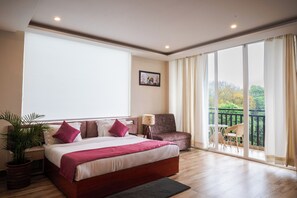 A bedroom with a large bed, a chair, a desk, and a balcony with a view.