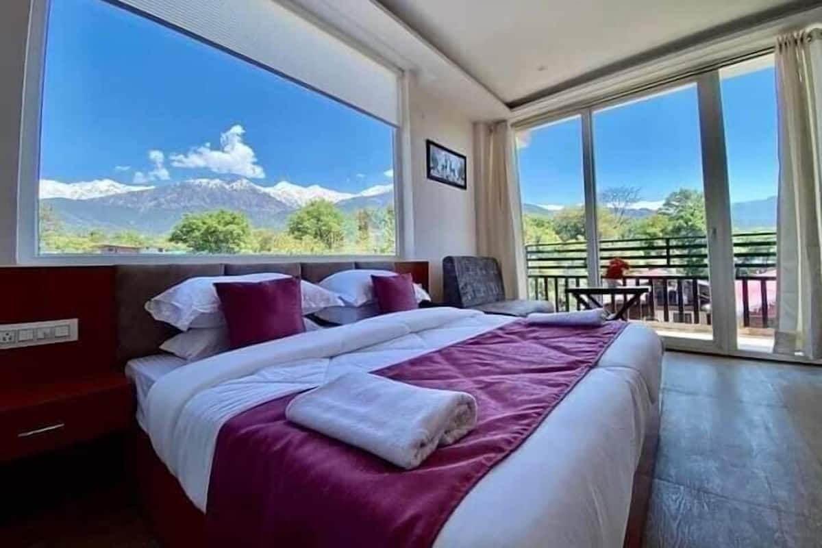 A bedroom with a large bed, a view of mountains, and a balcony with a table and chairs.