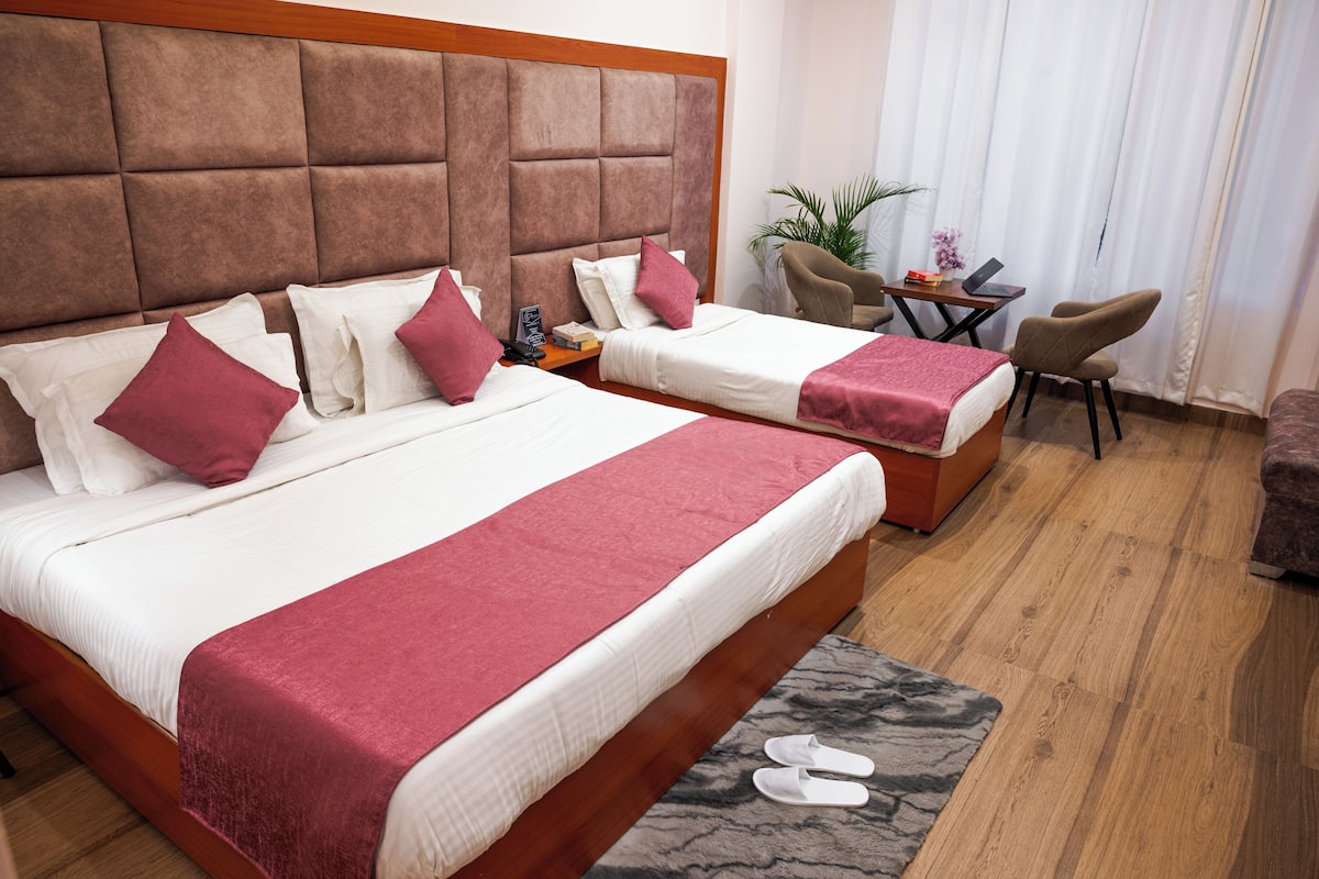A hotel room with two beds, a wooden headboard, a small table with a chair, and a plant.