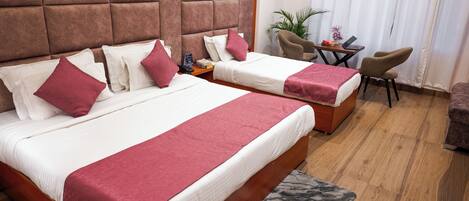 A hotel room with two beds, a wooden headboard, a small table with a chair, and a plant.