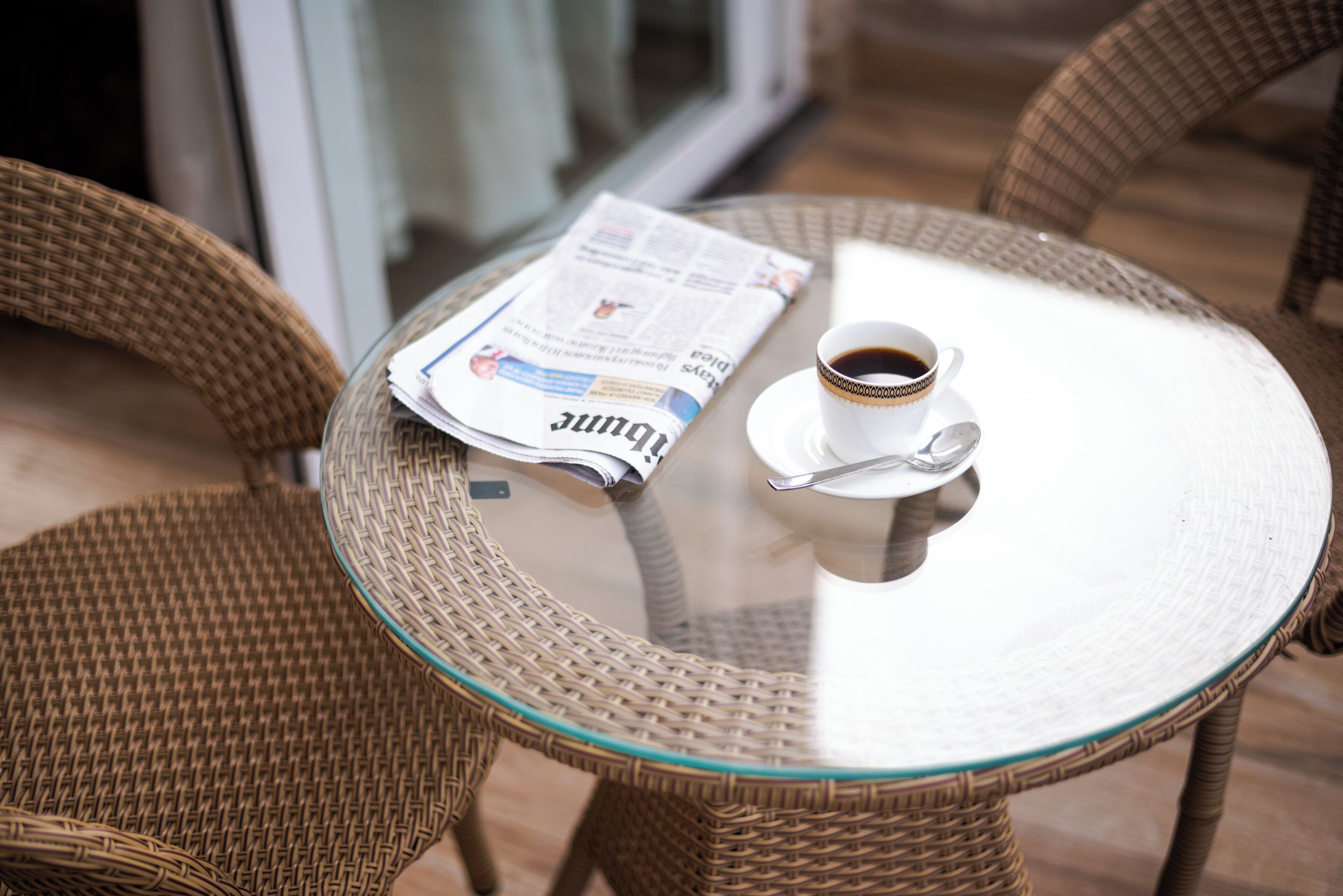 A glass-top table with a newspaper and a cup of coffee.