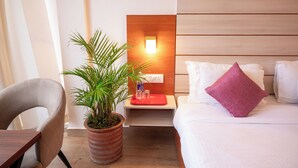 A hotel room with a bed, a nightstand with a red tray, a potted plant, and a chair. - Hotel Sagar Residency- Best Mountain View Hotel In Palampur (Palampur)