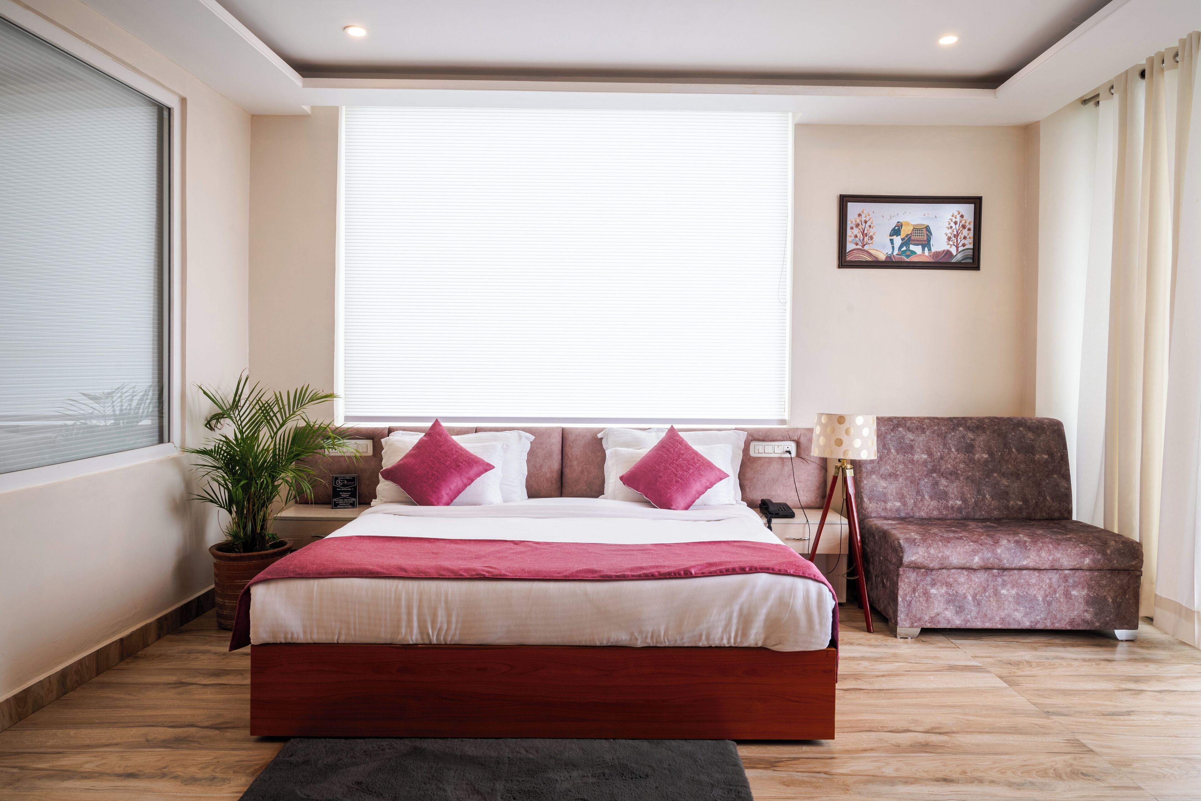 A bedroom with a large bed, a potted plant, a chair, and a wall-mounted lamp.
