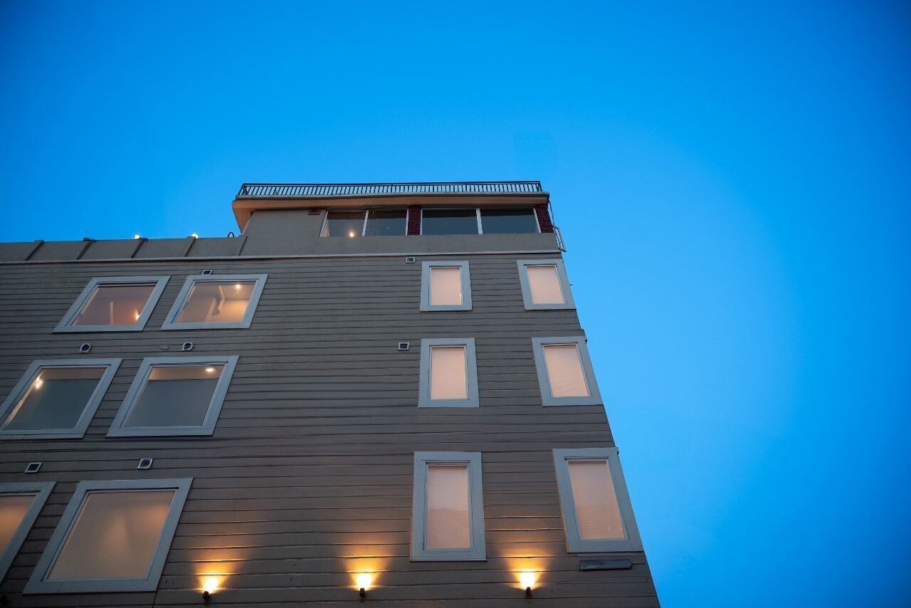 Un edificio de varios pisos con un diseño arquitectónico moderno, con ventanas regularmente distribuidas y un balcón en el piso superior.