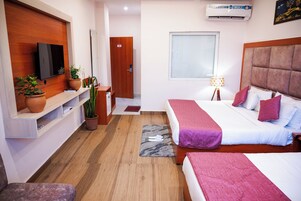 Habitación de hotel con una televisión montada en la pared, una cama con cabecera, una mesita de noche y un suelo de madera.
