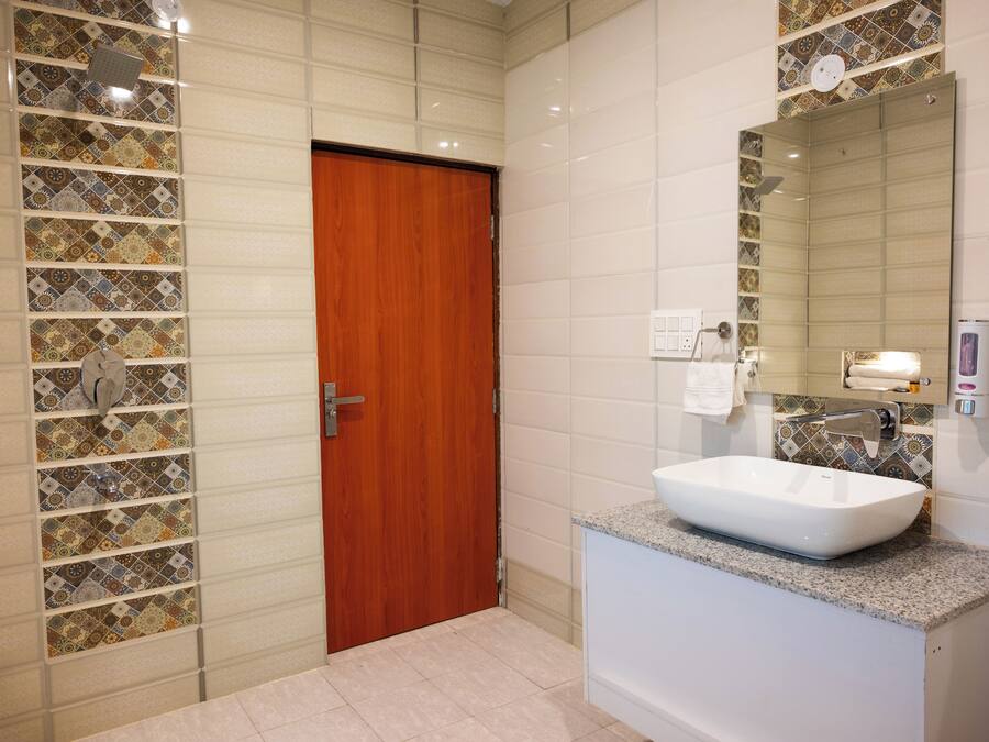 Ein Badezimmer mit Holztür, weißem Waschbecken und gefliestem Spritzschutz.