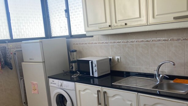 Een keuken met witte kastjes, een wasmachine, een magnetron en een spoelbak.