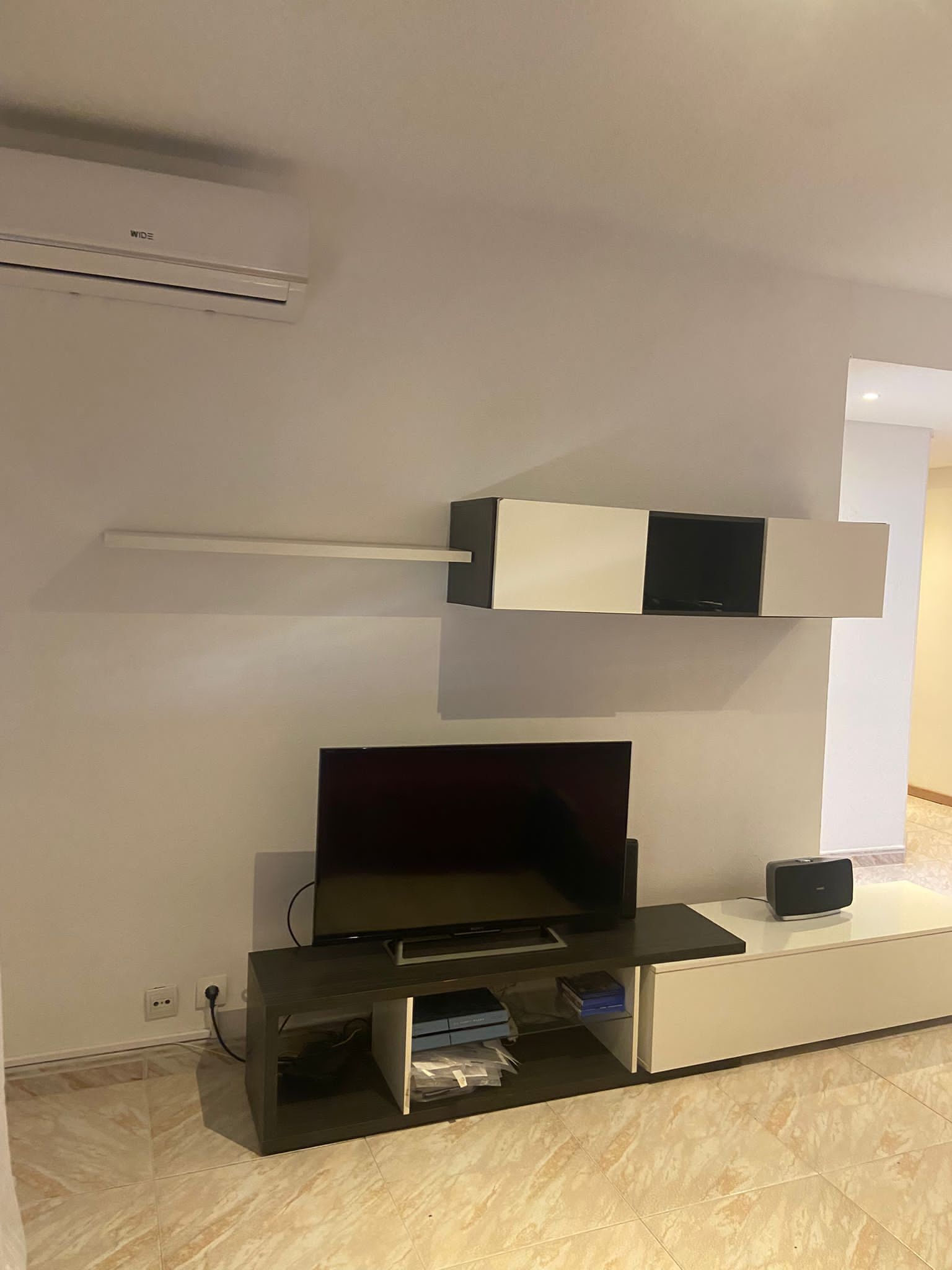 Een moderne woonkamer met een flatscreen-tv, een inbouwkast en een wandairconditioner.