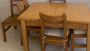 Een eetruimte met een houten tafel en stoelen, betegelde wanden en een raam met zonwering.