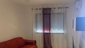 Een kamer met een rode bank, een televisie op een standaard en een raam met gordijnen.