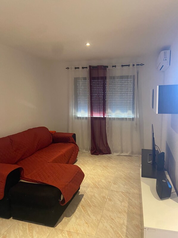 A room with a red sofa, a TV on a stand, and a window with curtains.
