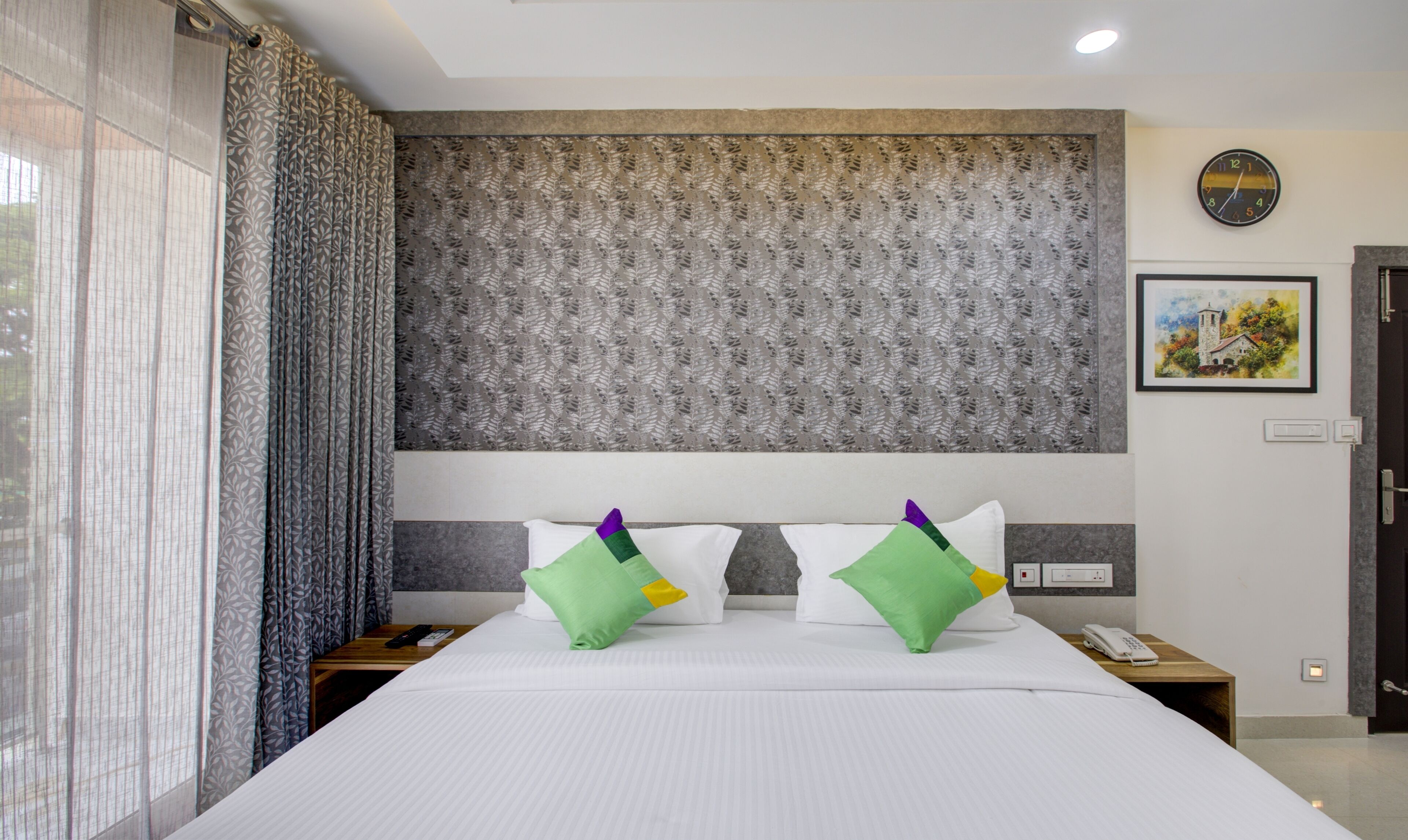 Une chambre d’hôtel avec un grand lit, deux tables de chevet, une horloge et un tableau au mur.