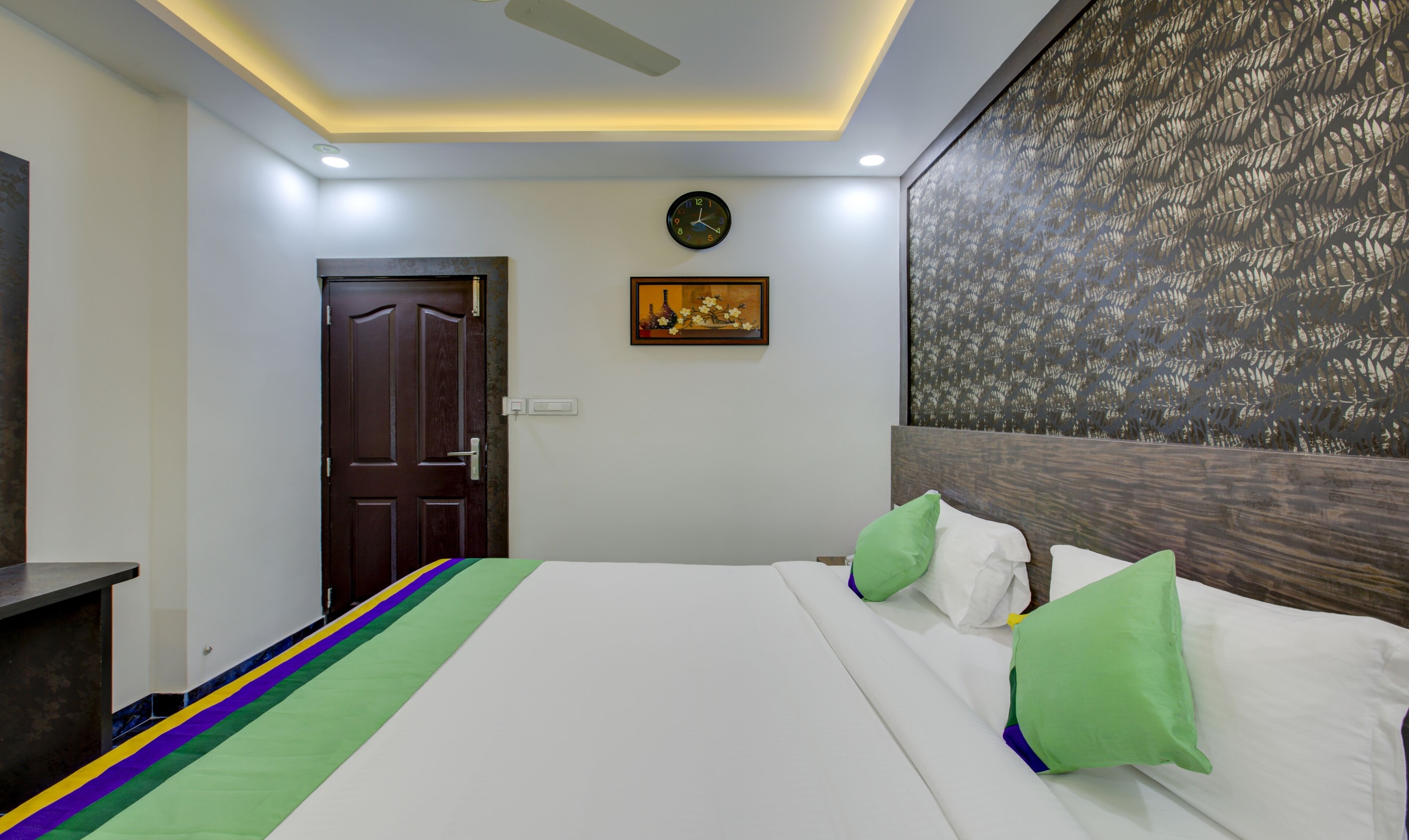 Une chambre d’hôtel avec un lit, une horloge, un tableau et un mur orné d’un motif.