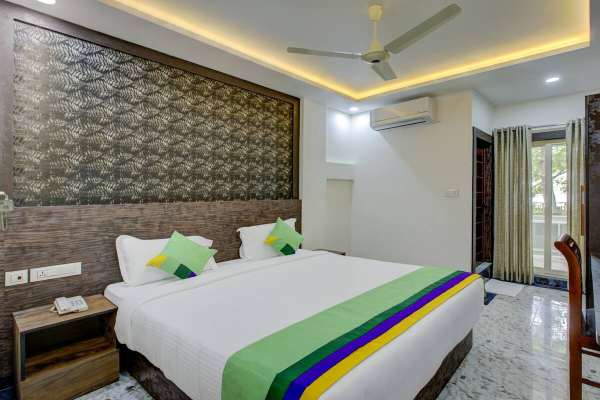 Quarto de hotel com cama, mesa de cabeceira, escrivaninha, cadeira e ventoinha no teto.