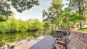 A wooden deck with chairs and tables overlooking a calm water body, surrounded by lush greenery and trees. - Spacious Tampa Vacation Rental w/ Pool & Dock (Tampa)