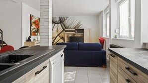 Une cuisine moderne dotée d’un lave-vaisselle intégré, un coin repas avec une chaise rouge et un canapé bleu dans l’espace salon.
