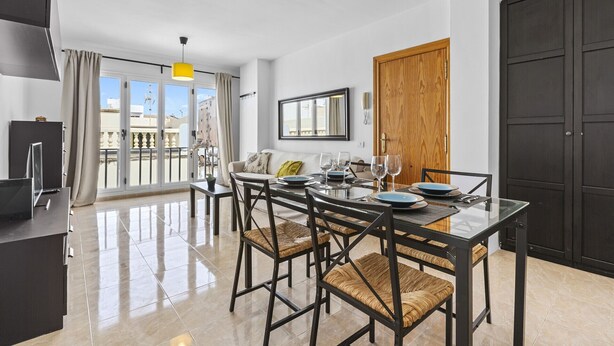 A modern dining area with a glass table, black chairs, and a view of the city through large windows. - Homely Lanzarote (Arrecife)