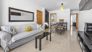 A modern living room with a sofa, coffee table, dining area, and kitchen in the background. - Homely Lanzarote (Arrecife)