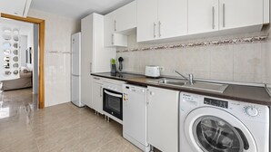 A modern kitchen with white cabinets, a built-in oven, a washing machine, and a sink. - Homely Lanzarote (Arrecife)