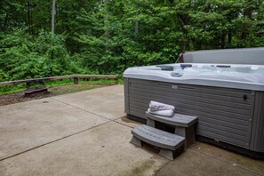 A hot tub with a bench and a towel, surrounded by a wooden deck and a forested area. - Bear Fork Lodge by The Inn & Spa at Cedar Falls (Logan)