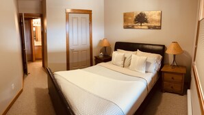 Quarto com cama, mesas de cabeceira, abajur e porta.