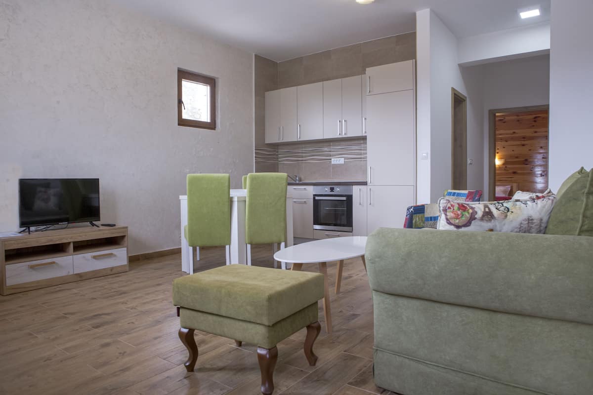 A modern living room with a flat-screen TV, green upholstered chairs, a white table, and a sofa.