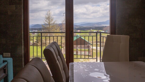 Habitación con vistas a un paisaje verde, balcón con barandilla y una mesa con una silla.