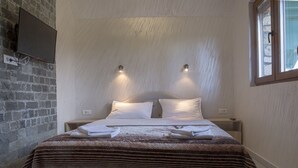 Una cama bien hecha con una colcha a rayas, dos mesitas de noche con lámparas, una pared de ladrillo y una ventana con persianas.
