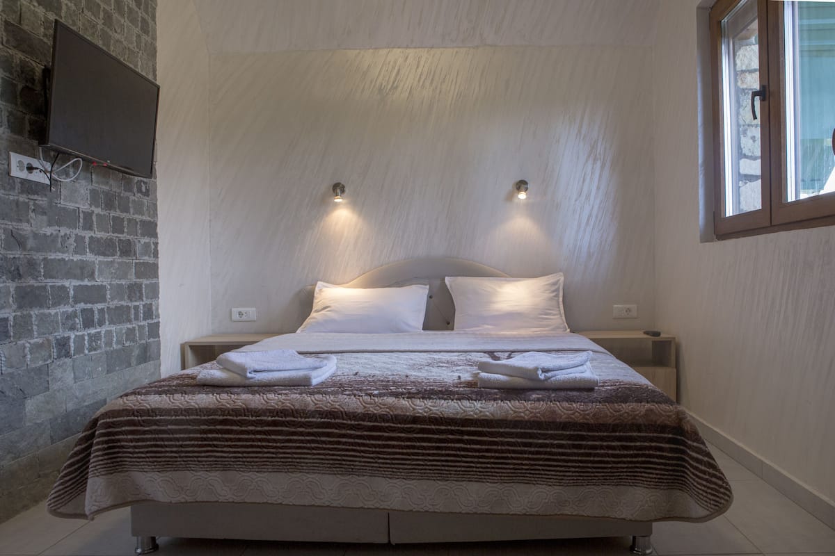 A neatly made bed with a striped blanket, two bedside tables with lamps, a brick wall, and a window with blinds.