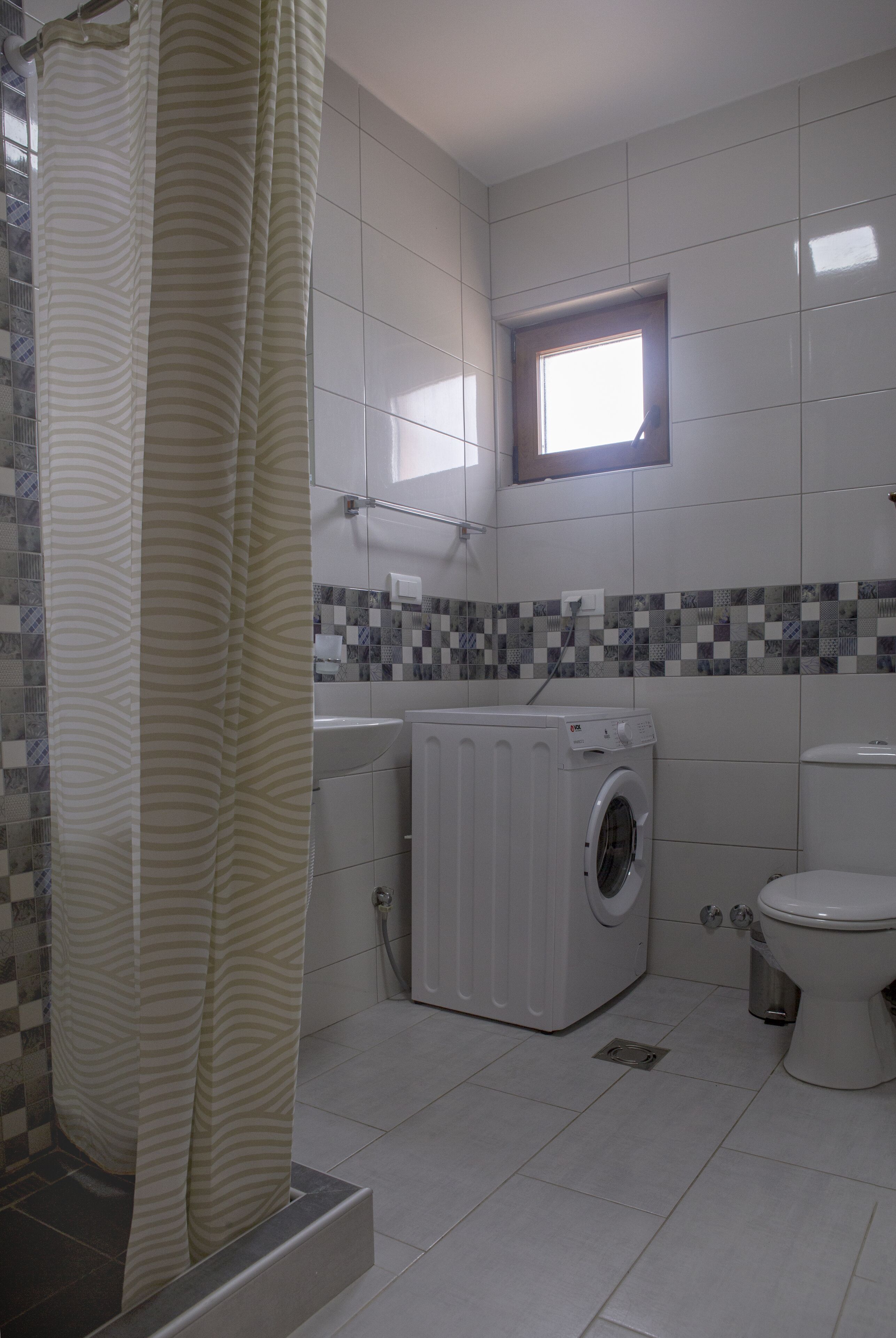 A bathroom with a washing machine, a toilet, and a shower curtain.