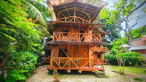 A multi-level wooden structure with a thatched roof, surrounded by lush greenery. - Don Jons Lodge -Surf & Yoga (Cóbano)